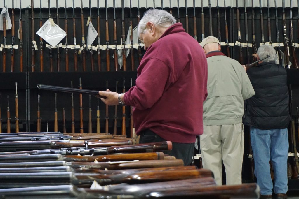 Man holding a long gun in the Rock Island Auction Company preview hall.