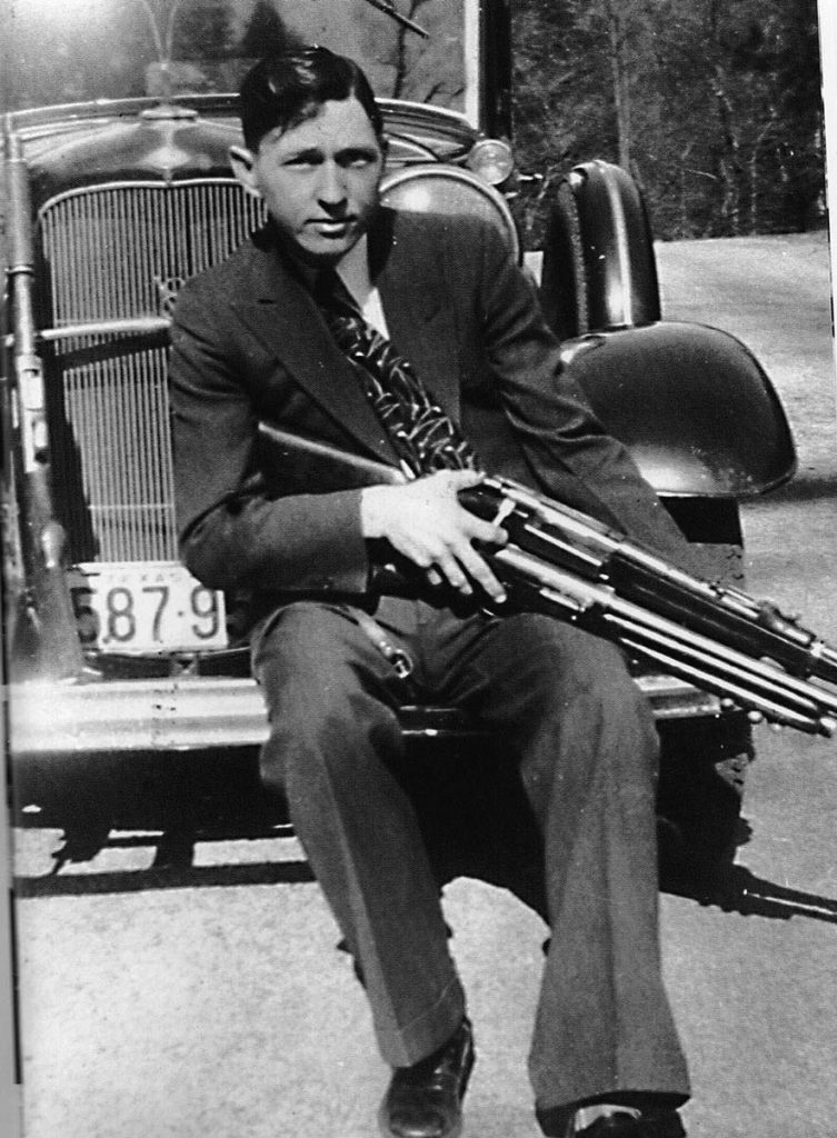 Clyde sitting on an old car with a gun across his lap